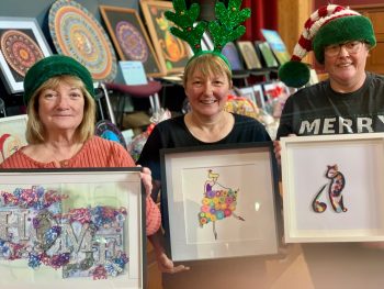 Three service users displaying their art at the christmas fair