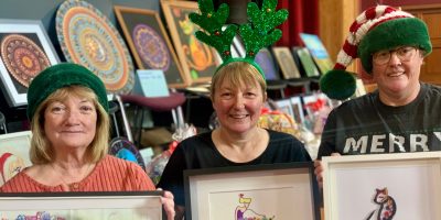 Three service users displaying their art at the christmas fair
